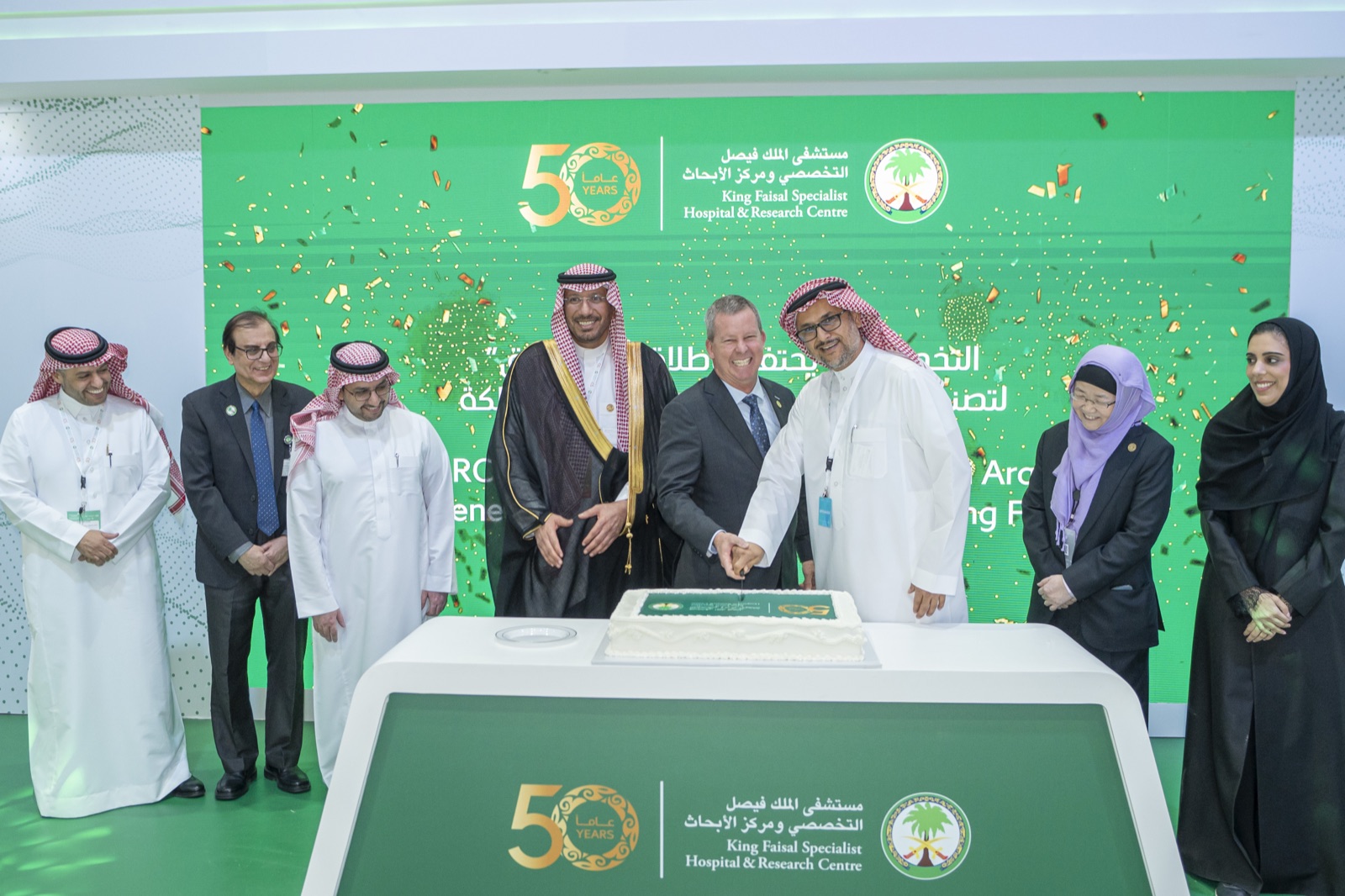 Senior KFSHRC leaders cutting the cake at the King Faisal Specialist Hospital & Research Centre 50-year anniversary celebration in Riyadh, beneath the institution's bilingual heritage signature and 50 Years insignia.
